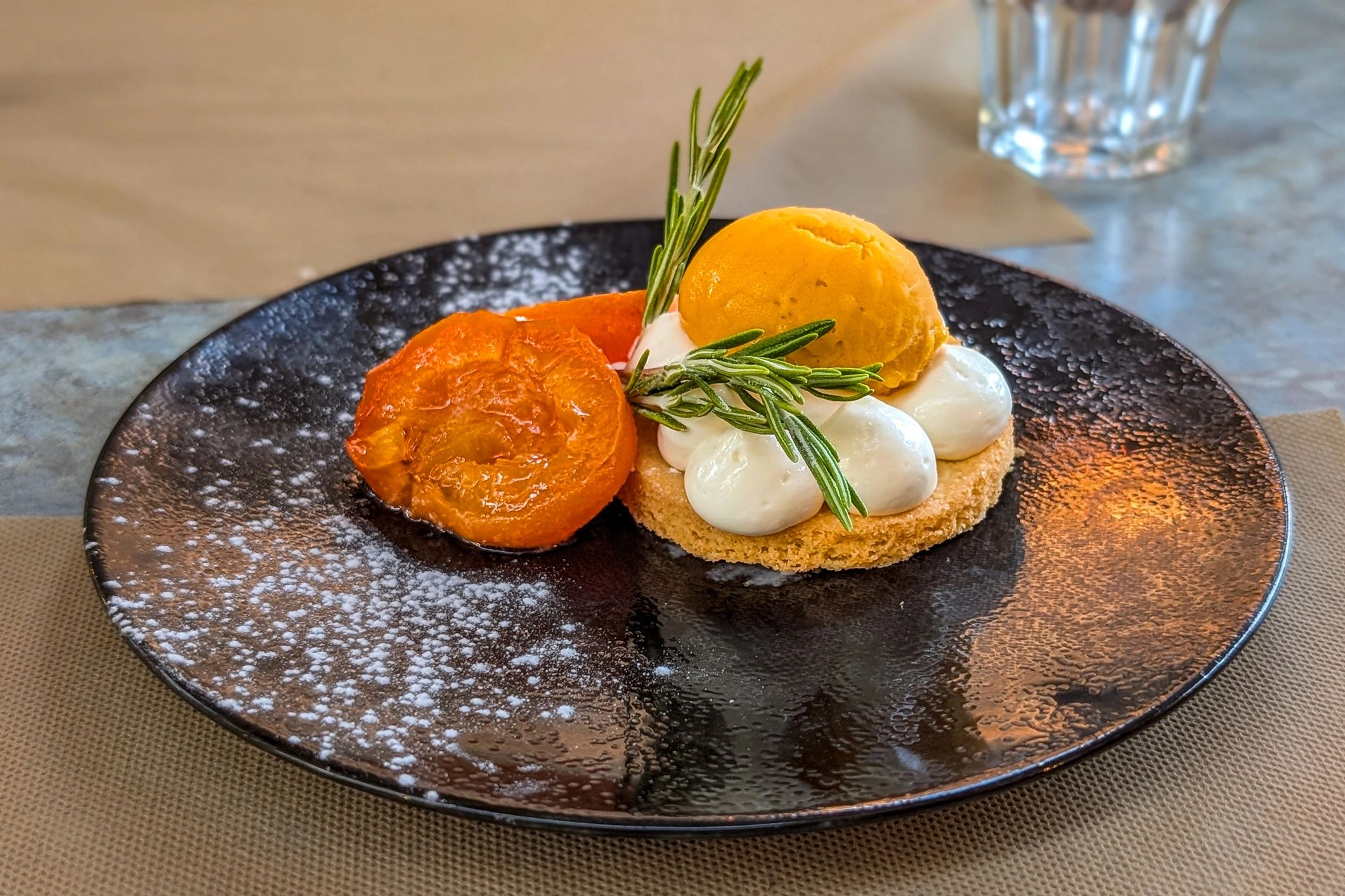 Apricot tart with poached apricots, cream base, and sorbet on a black plate